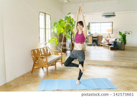 一位年輕的日本女性在客廳做瑜伽 一位年輕的日本女性在客廳做瑜伽 142573661