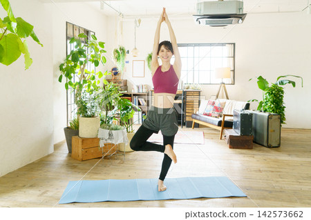 一位年輕的日本女性在客廳做瑜伽 一位年輕的日本女性在客廳做瑜伽 142573662