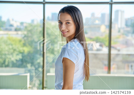 Young woman turning back and smiling near panoramic window portrait Young woman turning back and smiling near panoramic window portrait 142574139