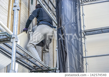 在房屋外牆翻新過程中安裝新壁板的工匠。 在房屋外牆翻新過程中安裝新壁板的工匠。 142574540