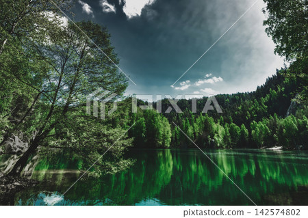Dark moody mountain lake, dense green forest. Mystery landscape with river and fir woods, sulking and silence scenery Dark moody mountain lake, dense green forest. Mystery landscape with river and fir woods, sulking and silence scenery 142574802