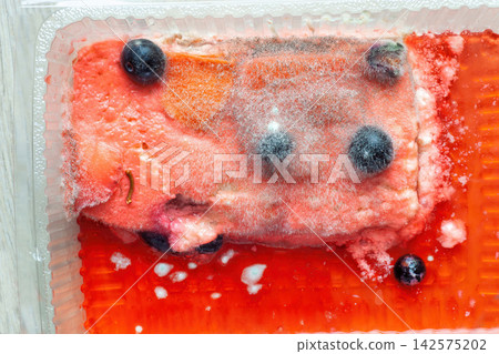Red fruit cake covered with white and black soft fungal mold, top view. Fluffy fungi spores mold growing on fruitcake Red fruit cake covered with white and black soft fungal mold, top view. Fluffy fungi spores mold growing on fruitcake 142575202