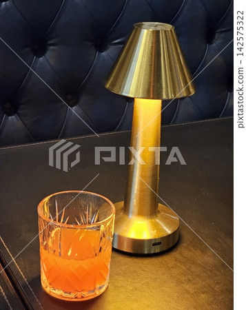 Orange Drink Beside Brass Table Lamp in Cozy Cafe Interior Orange Drink Beside Brass Table Lamp in Cozy Cafe Interior 142575322