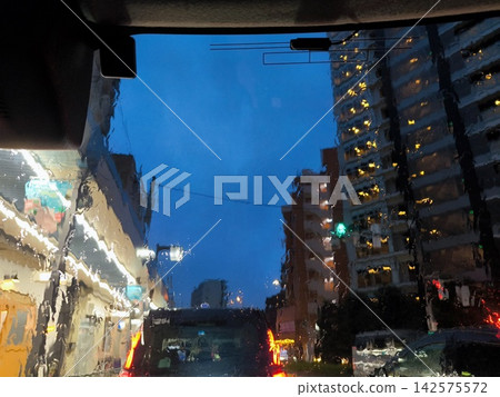 A view of the city skyline and the twilight blue sky from inside a car during a heavy rainstorm. 142575572