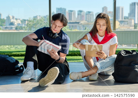 Two young students sitting on floor studying and taking notes near big window Two young students sitting on floor studying and taking notes near big window 142575590