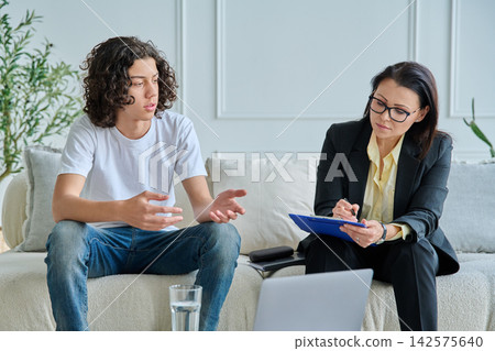 Psychologist listening to teenage boy in office Psychologist listening to teenage boy in office 142575640