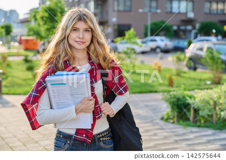 Young blonde female student holding textbooks and backpack outdoors in the city Young blonde female student holding textbooks and backpack outdoors in the city 142575644