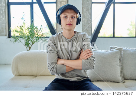 Young man in cap and headphones sitting on sofa Young man in cap and headphones sitting on sofa 142575657