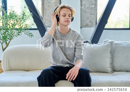 Young man listening to music in headphones at home Young man listening to music in headphones at home 142575658