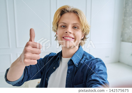 Happy teenage boy smiling at camera and showing thumbs up while taking selfie Happy teenage boy smiling at camera and showing thumbs up while taking selfie 142575675