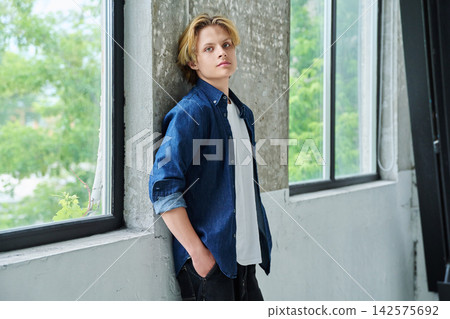 Handsome teenage boy looking at camera, near modern window Handsome teenage boy looking at camera, near modern window 142575692