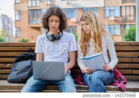 Teen students studying with laptop on bench outdoor Teen students studying with laptop on bench outdoor 142575698