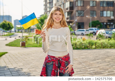 Smiling young woman holding Ukrainian flag outdoors 142575700