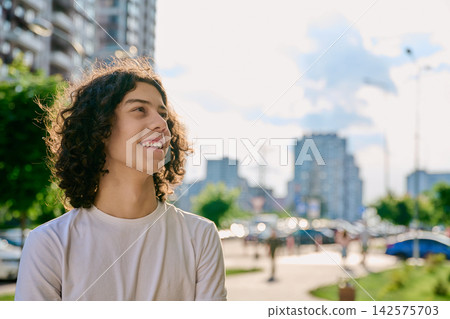 Happy teen boy with curly hair looking away outdoor Happy teen boy with curly hair looking away outdoor 142575703