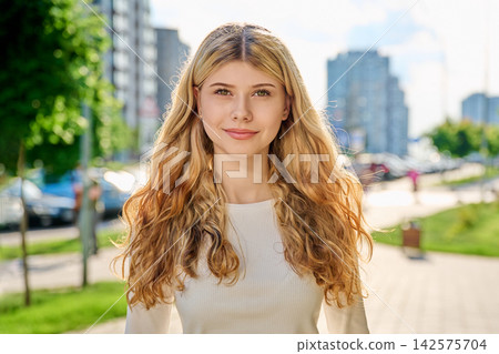 Smiling blonde girl looking at camera on city street Smiling blonde girl looking at camera on city street 142575704