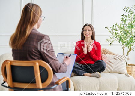 Young woman sits on sofa, gesturing expressively while talking to her therapist 142575705