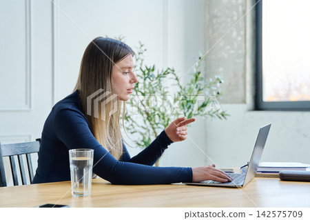 Young woman using laptop for video chat sitting at a table Young woman using laptop for video chat sitting at a table 142575709