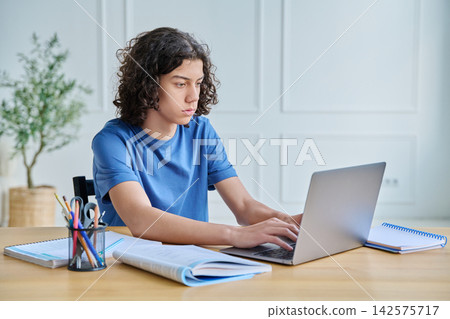 Focused teenage boy studying on laptop at home desk Focused teenage boy studying on laptop at home desk 142575717