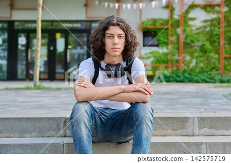 Serious young student with headphones sitting outside Serious young student with headphones sitting outside 142575719