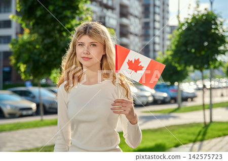Beautiful young woman holding small flag of Canada Beautiful young woman holding small flag of Canada 142575723
