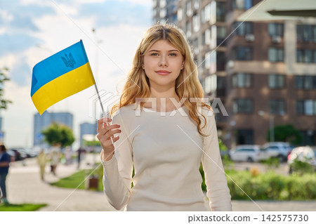 Smiling young woman holding Ukrainian flag outdoors Smiling young woman holding Ukrainian flag outdoors 142575730
