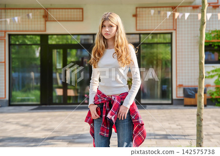 Serious 16 year old blonde teenage girl standing outdoors Serious 16 year old blonde teenage girl standing outdoors 142575738