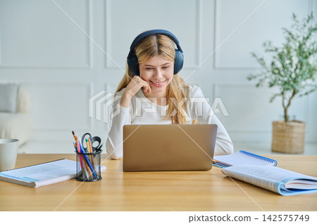 Happy teenage girl in headphones studying with laptop Happy teenage girl in headphones studying with laptop 142575749