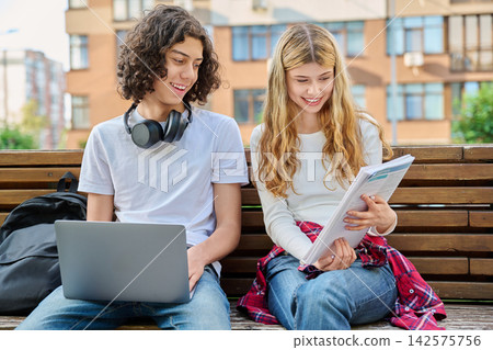 Teen students studying with laptop on bench outdoor Teen students studying with laptop on bench outdoor 142575756
