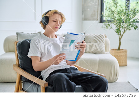 Teenage student in headphones reading book indoor Teenage student in headphones reading book indoor 142575759