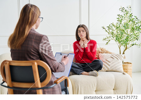 Sad teenage female patient in therapy session in psychologist office. Professional mental support Sad teenage female patient in therapy session in psychologist office. Professional mental support 142575772