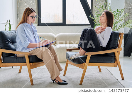 Professional female psychologist taking notes during a consultation with a young female client 142575777