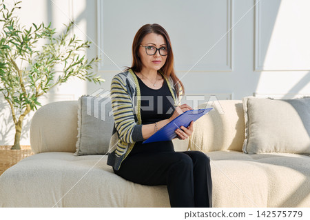Portrait of professional psychologist therapist woman taking notes on clipboard in office Portrait of professional psychologist therapist woman taking notes on clipboard in office 142575779