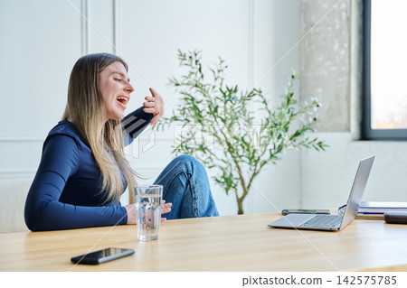 Young woman using laptop for video chat sitting at a table Young woman using laptop for video chat sitting at a table 142575785