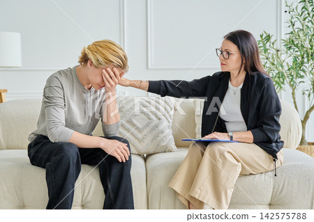 Female psychologist comforting and supporting a sad teenage boy during therapy session Female psychologist comforting and supporting a sad teenage boy during therapy session 142575788