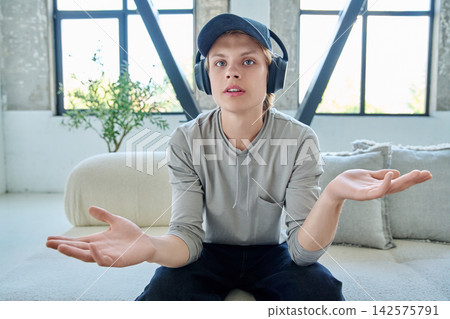 Teen boy in headphones talking via webcam on couch 142575791