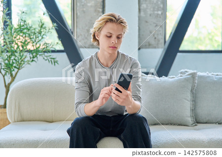 Young man using smartphone on sofa in modern home Young man using smartphone on sofa in modern home 142575808