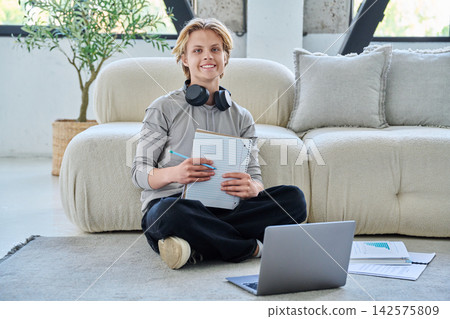 Young smiling male student studying with laptop on floor at home Young smiling male student studying with laptop on floor at home 142575809