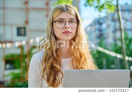 Serious teen student with glasses and laptop on campus Serious teen student with glasses and laptop on campus 142575817