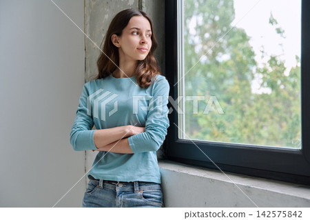 Pensive teen girl with crossed arms looking out window Pensive teen girl with crossed arms looking out window 142575842
