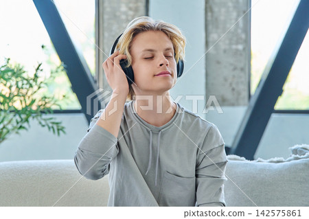 Young man listening to music in headphones at home Young man listening to music in headphones at home 142575861