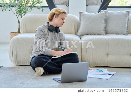 Young student studying with laptop on floor at home Young student studying with laptop on floor at home 142575862