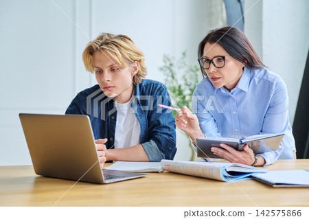 Teenage student and teacher looking at laptop indoor Teenage student and teacher looking at laptop indoor 142575866