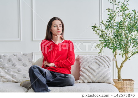 Portrait of beautiful, dreaming, pensive young teenage girl sitting on sofa Portrait of beautiful, dreaming, pensive young teenage girl sitting on sofa 142575870