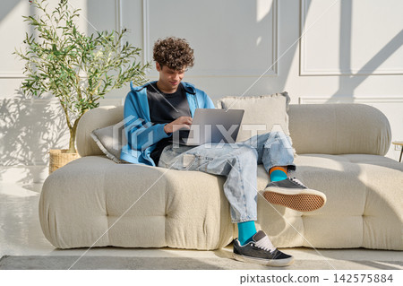 Portrait handsome young male typing on laptop sitting on sofa at home 142575884