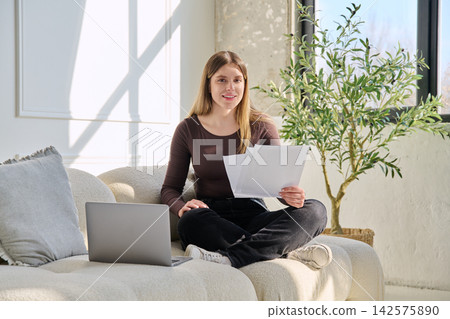 Smiling young woman with business, educational important papers, laptop in home 142575890