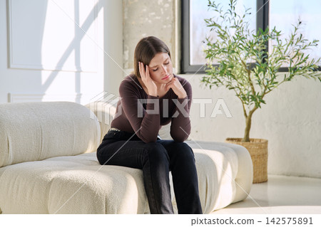 Unhappy upset stressed young woman sitting on sofa at home Unhappy upset stressed young woman sitting on sofa at home 142575891