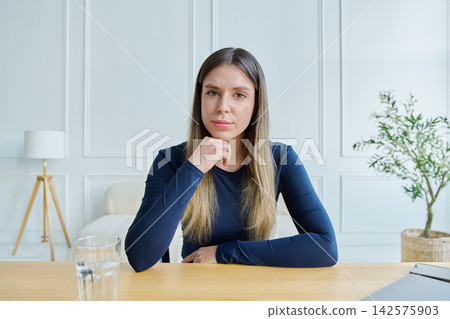 Webcam portrait female university student, sitting at the table with textbooks Webcam portrait female university student, sitting at the table with textbooks 142575903