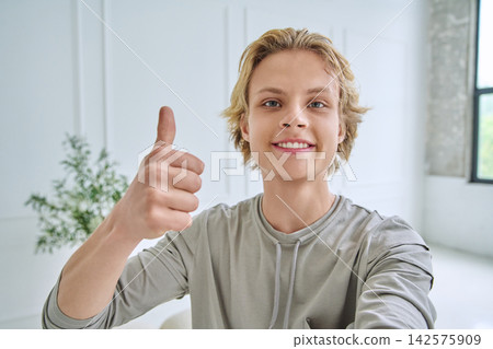 Happy teenage boy smiling at camera and showing thumbs up while taking selfie Happy teenage boy smiling at camera and showing thumbs up while taking selfie 142575909