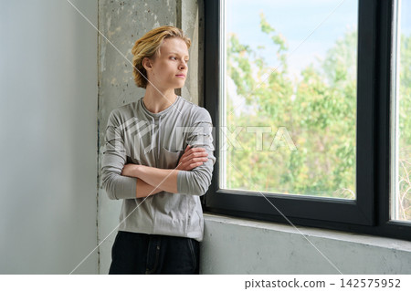 Thoughtful teenage boy with crossed arms by window 142575952