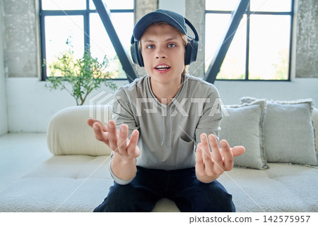 Teen boy in headphones talking via webcam on couch Teen boy in headphones talking via webcam on couch 142575957